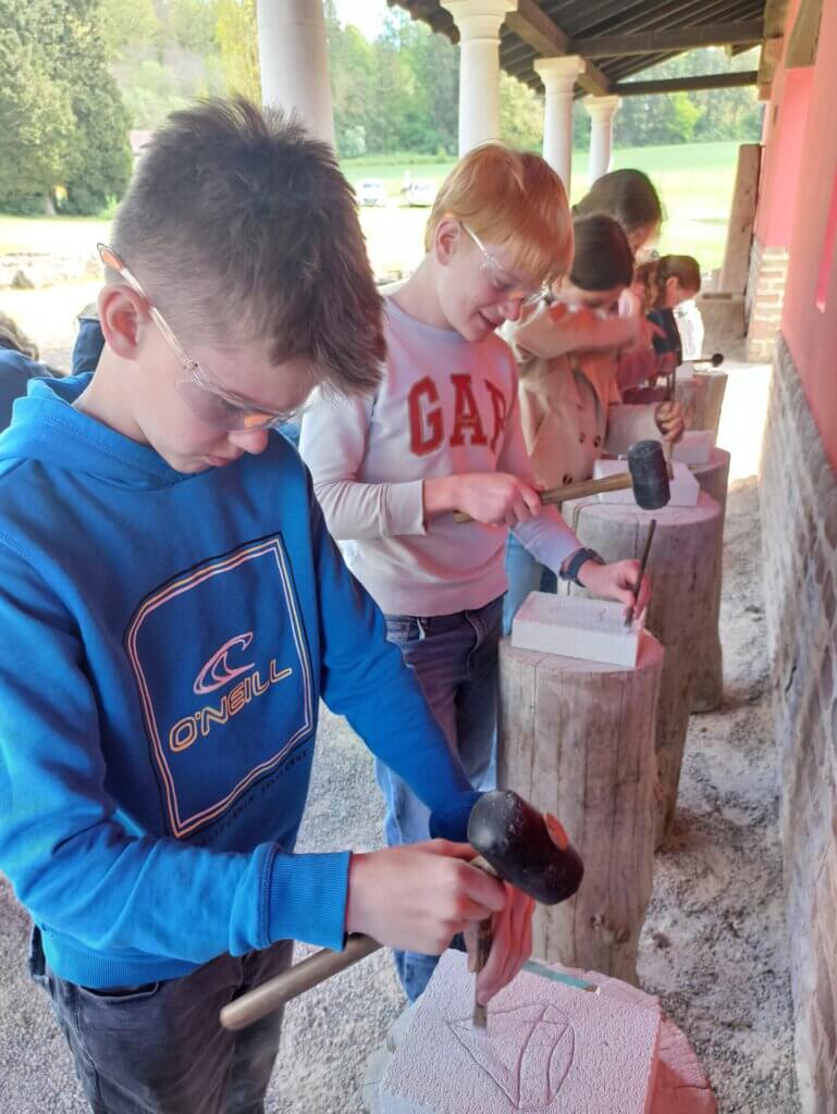Lateinschüler bearbeiten beim Römerausflug Steine mit Hammer und Meißel