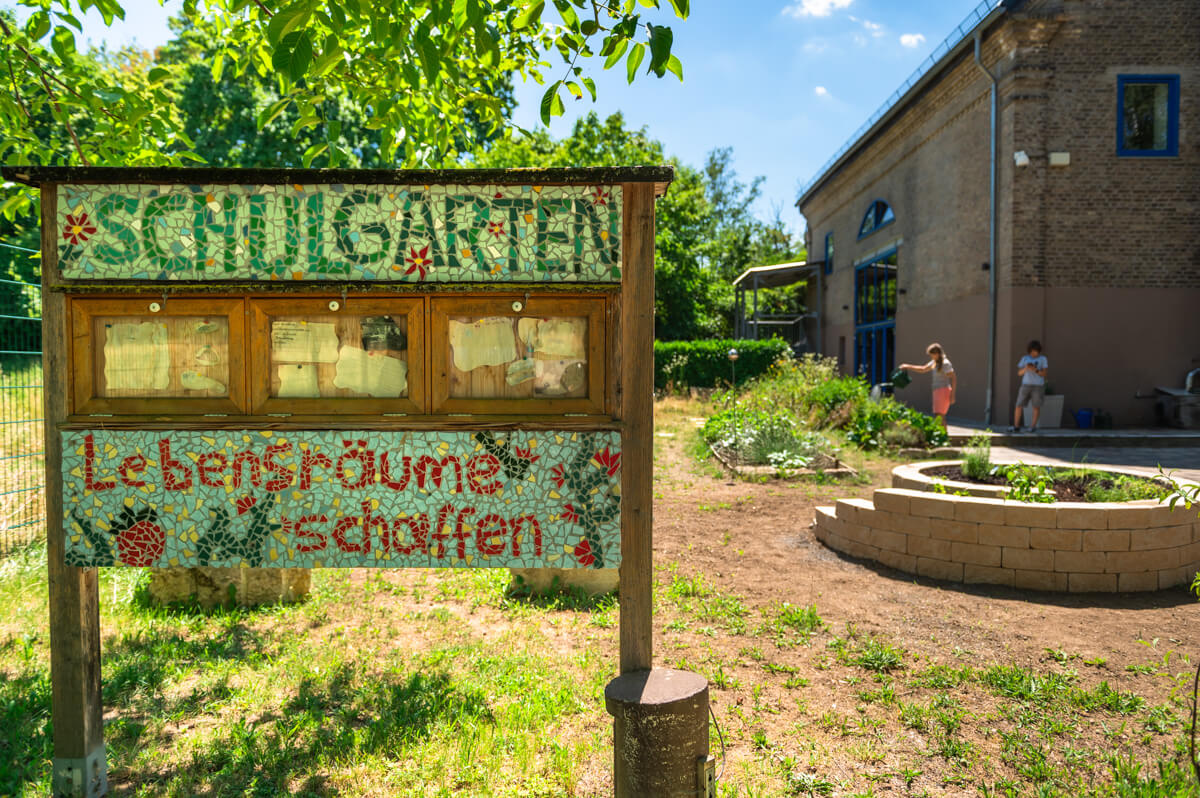 Schulgarten der Humboldt-Schule mit Beeten und Mosaikschild